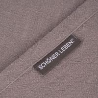 75623-SCHoeNER-LEBEN--Tischlaeufer-Bio-Ramie-Leinenoptik-grau-40x160cm-KW36-2021-161421Capture0002.jpg Nahaufnahme des gewebten Labels SCHÖNER LEBEN. auf grauem Tischläuferstoff mit Label und Saum