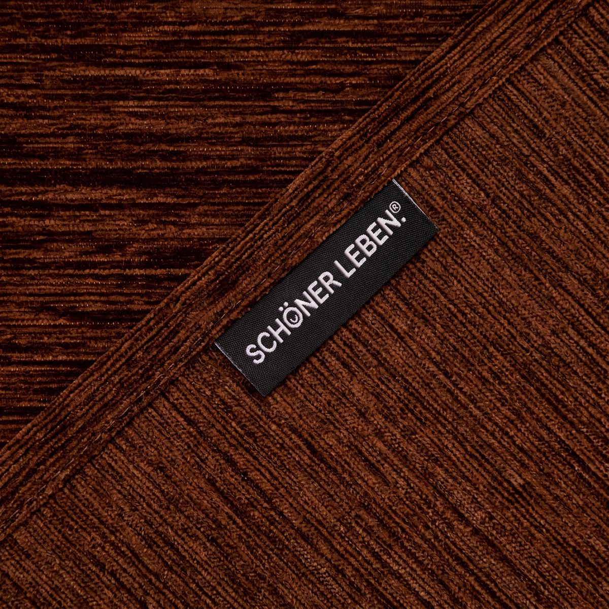 Ecke eines braunen Chenille-Stoffs mit sichtbarem Webetikett, diagonale Stoffanordnung, samtige Textur