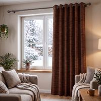 Wohnzimmer mit braunem Thermovorhang aus Chenille mit Ösen, Sessel und Pflanzen vor verschneitem Fenster