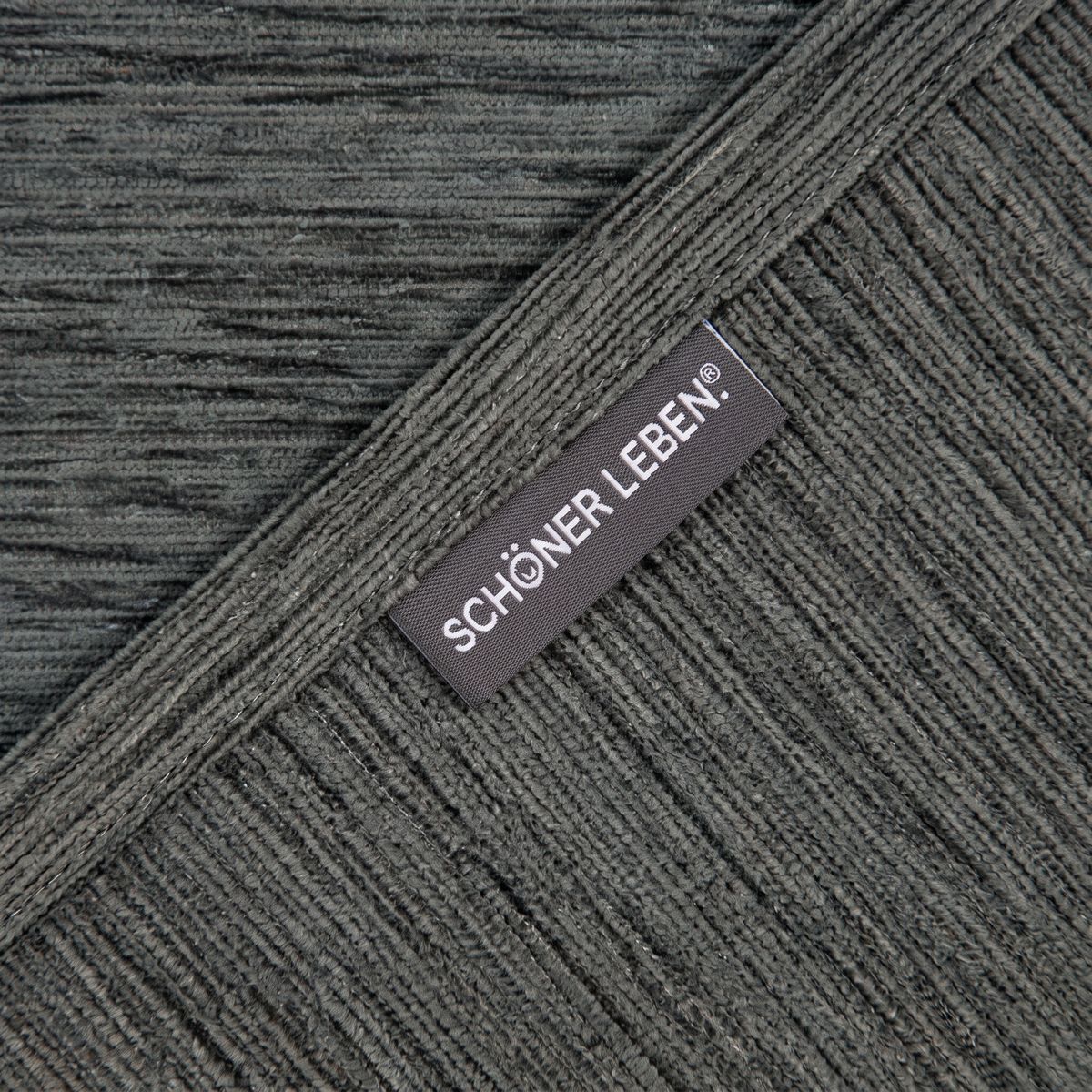 Textilanhänger SCHÖNER LEBEN auf strukturiertem blaugrauem Chenille Stoff, diagonale Stoffanordnung
