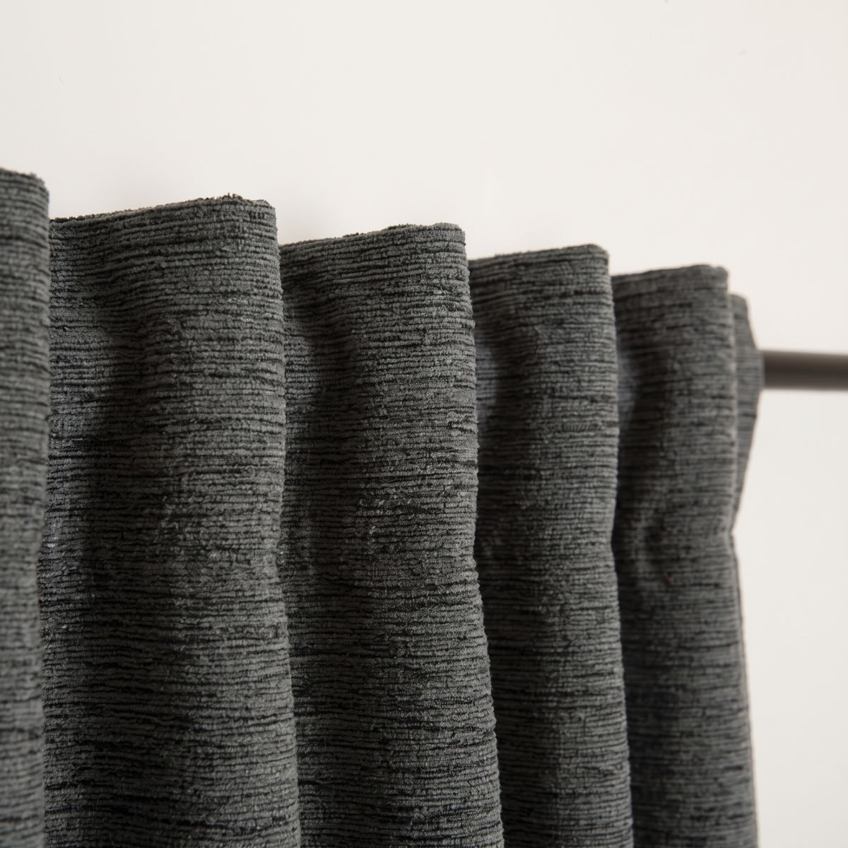 faltenreicher Vorhang aus strukturierter Chenille in blaugrau an einer Gardinenstange, neutrale Wand im Hintergrund