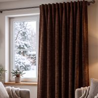 brauner Thermovorhang aus Chenille vor einem Fenster, Wohnzimmer mit Sofaecke und Topfpflanze im winterlichen Ambiente