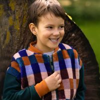 Junge trägt Jacke mit Würfelmuster aus Teddyplüsch in lila, orange, grün