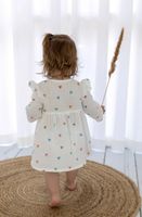 Kleinkind mit einem luftigen Sommerkleid aus Musselin Stoff mit buntem Herzchenmuster, fotografiert von hinten vor weißen Vorhängen Kleid Rueckseite
