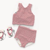 Kinder-Badeoutfit aus rosa Badeanzugstoff mit weißen Punkten neben Flip-Flops arrangiert