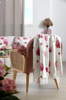Wohndecke mit pinkem Blumenmuster und Fransen über einem Stuhl im gemütlich dekorierten Wohnzimmer