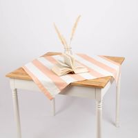 Tischdecke mit peach-ecru Streifen stilvoll dekoriert mit Vase und Buch auf Holztisch.