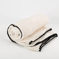 Superflauschige Kuscheldecke Jade in Dove White, 130x180 cm groß, zusammengerollt mit schwarzem Kettelrand und Verpackungsband von Unique Living - Nahaufnahme