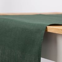 Grüner Leinen-Tischläufer Erik, präsentiert auf Holztisch als natürlicher, nachhaltiger Läufer im Format 47×150 cm - von der Seite