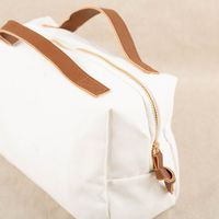 Praktische, unifarbene Kosmetiktasche Travel aus weißem Baumwoll-Canvas. Die Tasche mit Reißverschluss und braunen Tragegriffen ist 26 mal 12 mal 17 Zentimeter groß - von der Seite