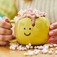 Keramiktasse „Happy Mug“ von Sass & Belle in leuchtendem Gelb. Die bauchige Tasse mit Henkel ist handbemalt und trägt ein aufgedrucktes, freundliches Smiley-Gesicht. Sie ist eine dekorative und fröhliche Ergänzung für jede Küche - mit überlaufender heißer 