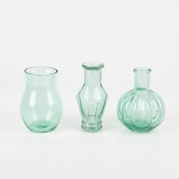 Dekoratives Vasen-Set von Sass & Belle aus recyceltem, transparentem, leicht türkisem Glas. Das Set enthält drei unterschiedliche Flaschenformen mit Rillen-Details. Die Vasen sind jeweils etwa 8×10 cm groß und eignen sich ideal für kleine Blumenarrangement