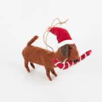 Niedlicher, handgearbeiteter Deko-Anhänger von Sass & Belle in Dackel-Form. Der braune Filz-Hund trägt eine rote Weihnachtsmütze und hält eine Zuckerstange im Maul. Der kuschelige Anhänger ist 10×14 cm groß und wird von einer Juteschnur gehalten - Vollansi