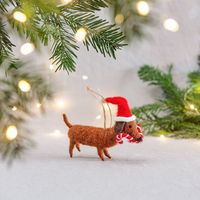 Niedlicher, handgearbeiteter Deko-Anhänger von Sass & Belle in Dackel-Form. Der braune Filz-Hund trägt eine rote Weihnachtsmütze und hält eine Zuckerstange im Maul. Der kuschelige Anhänger ist 10×14 cm groß und wird von einer Juteschnur gehalten - in Szene