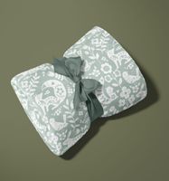 92775-Teddy-Stoff-Pluesch-ALIO-Blumen-Ornamente-schwarz-lila-blau-1-50m-Breite-Screenshot-2025-10-02-143405.jpg Gefalteter mintgrüner Fleecestoff mit weißem Tier- und Blumenmuster, mit Schleife gebunden