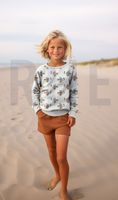 Kind am Strand im wollweißen Sweatshirt mit Dackel-mit-Mütze-Motiv; French-Terry-Stoff, elastische Bündchen sichtbar.