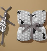 Grauer, kuschelweicher Fleecestoff, präsentiert mit schwarzen und weißen Katzenmotiven, weißen Punkten und Schriftzügen als verspieltes Design, 1,45 m breit - mit Kuscheltier als Geschenk praesentiert