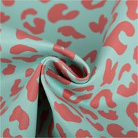 Mintfarbenes Kunstleder „Happy Leo“, präsentiert mit korallrotem Leopardenmuster von Cherry Picking by Swafing für moderne DIY-Projekte - kunstvoll eingedreht in Falten