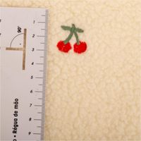 Teddystoff Boucle wollweiß mit Kirschen Stickerei. Das Muster zeigt rote Kirschen auf der flauschigen Stoffoberfläche. Breite 145cm - mit Massband