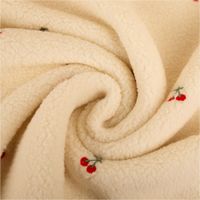 Teddystoff Boucle wollweiß mit Kirschen Stickerei. Das Muster zeigt rote Kirschen auf der flauschigen Stoffoberfläche. Breite 145cm - kunstvoll drapiert