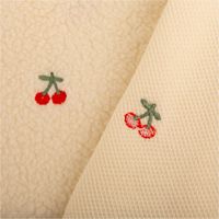 Teddystoff Boucle wollweiß mit Kirschen Stickerei. Das Muster zeigt rote Kirschen auf der flauschigen Stoffoberfläche. Breite 145cm - mit Rueckseite