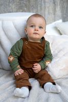 93205-French-Terry-Loewe-gruen-Sommersweat-mit-Schlingenstruktur-150cm-24407-027-6.jpg Baby trägt Shirt aus grünem Löwen-French-Terry unter brauner Latzhose