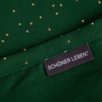 SCHÖNER LEBEN. Markenlabel auf grünem Tischläufer mit goldenen Punkten.