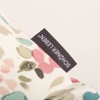 Detail des Markenlabels SCHÖNER LEBEN. an der Kissenhülle mit Aquarell-Blütenmuster.