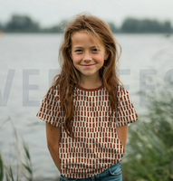 93857-Jersey-Stoff-Bio-Baumwolljersey-Baerchen-natur-1-48m-Breite-Screenshot-2026-02-21-220714.png Kind trägt ein T-Shirt aus Bio-Baumwolljersey mit braunem Streifenmuster auf naturfarbenem Grund am See