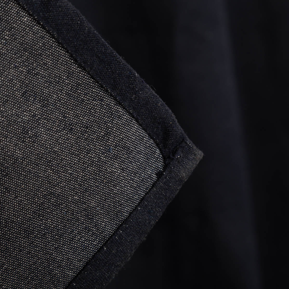 Vorhang Ösenvorhang Maritim Möwen jeansblau meliert weiß 140x260cm Detailaufnahme eines schwarzen Baumwollstoffs mit Rand in Grau-Schwarz-Kontrast.