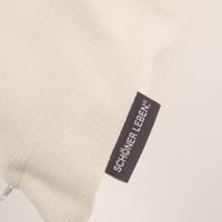 Nahaufnahme der Outdoor-Kissenhülle in Ecru-Weiß mit SCHÖNER LEBEN.-Label und strukturierter Oberfläche.