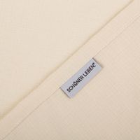 Nahaufnahme eines beigen Stoffes mit feiner Webstruktur und dem Label SCHOENER LEBEN.
