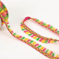 Farbige Flechtborte mit Quastenfransen in Pink, Gelb und Grün auf Rolle ausgelegt