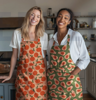 Canvas-Baumwollstoff, 138 cm breit, in hellem Peach-Orange mit großflächigen, locker verteilten Orangen in sattem Orange mit olivgrünen Blättern – frisch, fruchtig und sommerlich-mediterran - als Schuerze getragen
