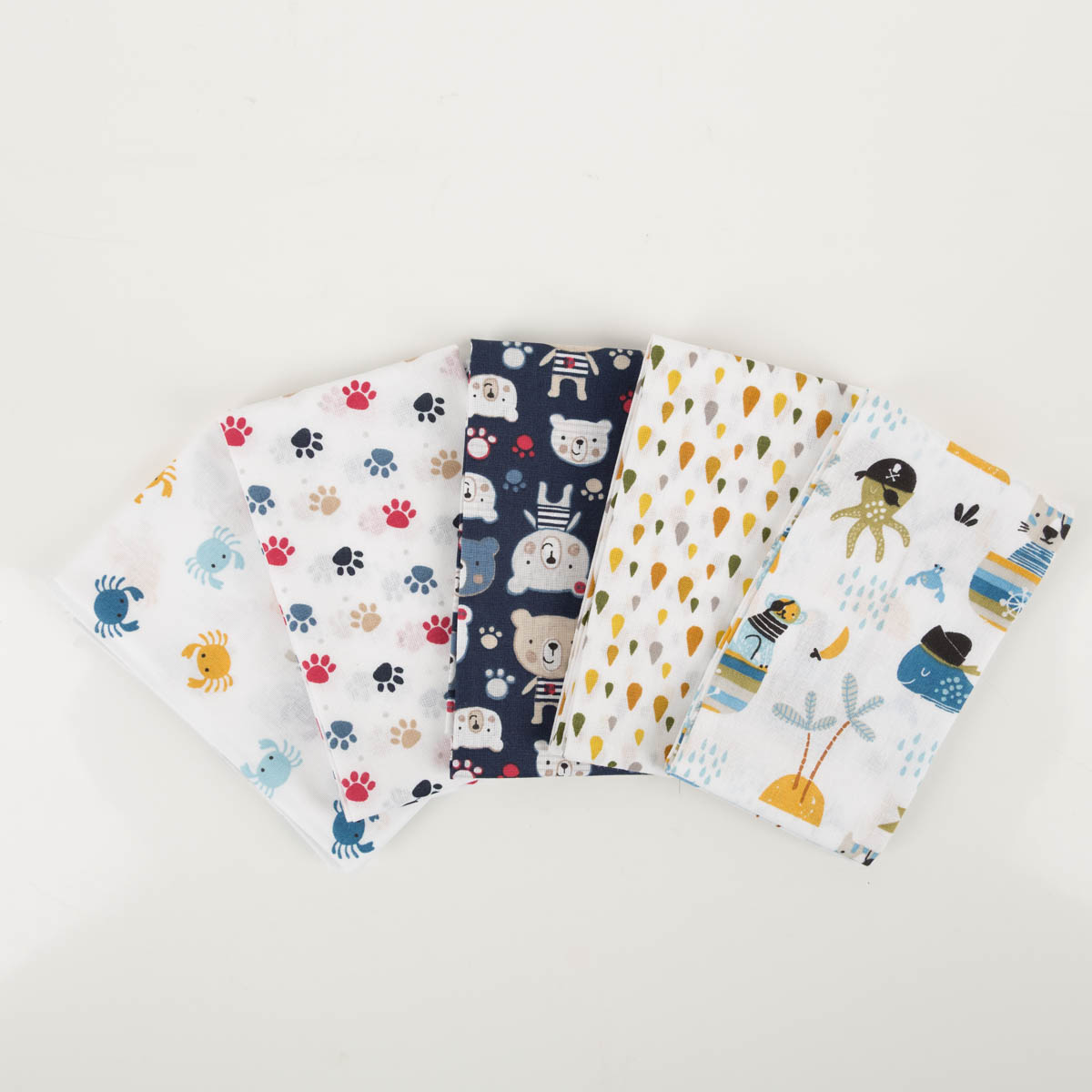 Kinder-Patchworkset mit fünf Baumwollstoffen in Weiß und Blau, mit Krabben, Tatzen, Bären, Tropfen und Piratenmotiven.