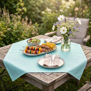 Outdoor-Mitteldecke in Uni Blau mit wasserabweisender Struktur auf Gartentisch mit sommerlicher Tischdekoration.