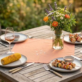 Outdoor Mitteldecke 85x85 cm in Orange, wasserabweisend, dekoriert auf einem Gartentisch mit Geschirr und Blumen.