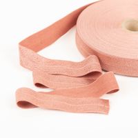 YKK elastisches Falzband / Falzgummi 20mm gelbbraun (20-m-Box) Rolle und Verlauf eines rosafarbenen Textilbands auf hellem Untergrund, zeigt Detail der Textur.