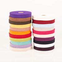 YKK elastisches Falzband / Falzgummi 20mm rohweiß (20-m-Box) Bunte Stoffrollen gestapelt, detailreiche Ansicht der Farbkombinationen von Lila bis Creme.