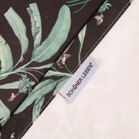 Vorhang Baumwolle Blumen Palmenblätter schwarz bunt mit Smok-Schlaufenband 245x130cm Detailaufnahme einer Kante mit floralem Muster auf dunklem Stoff, hellem Hintergrund und SCHOENER LEBEN Etikett.