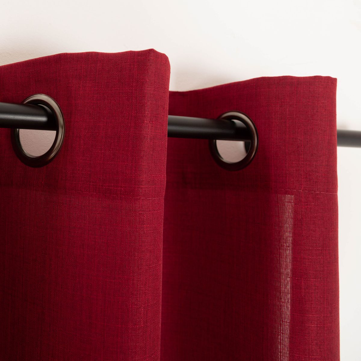 Roter Vorhang an schwarzer Stange mit gleichmäßiger Struktur und elegantem Faltenwurf.