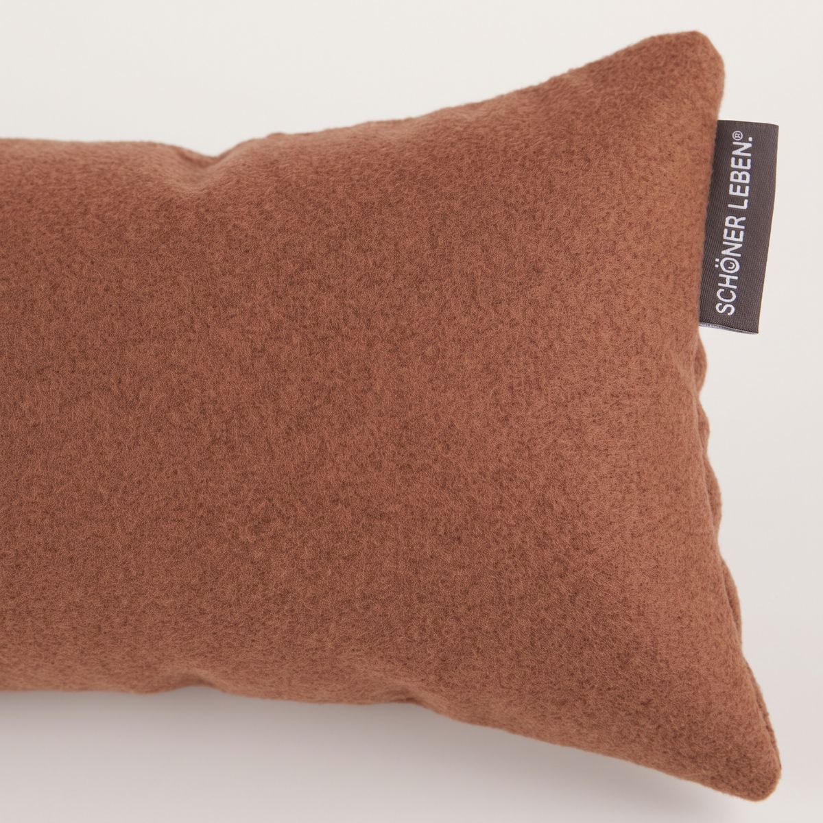 Nahaufnahme eines Zugluftstoppers aus rostbraunem Fleece mit sichtbarem SCHÖNER LEBEN. Label