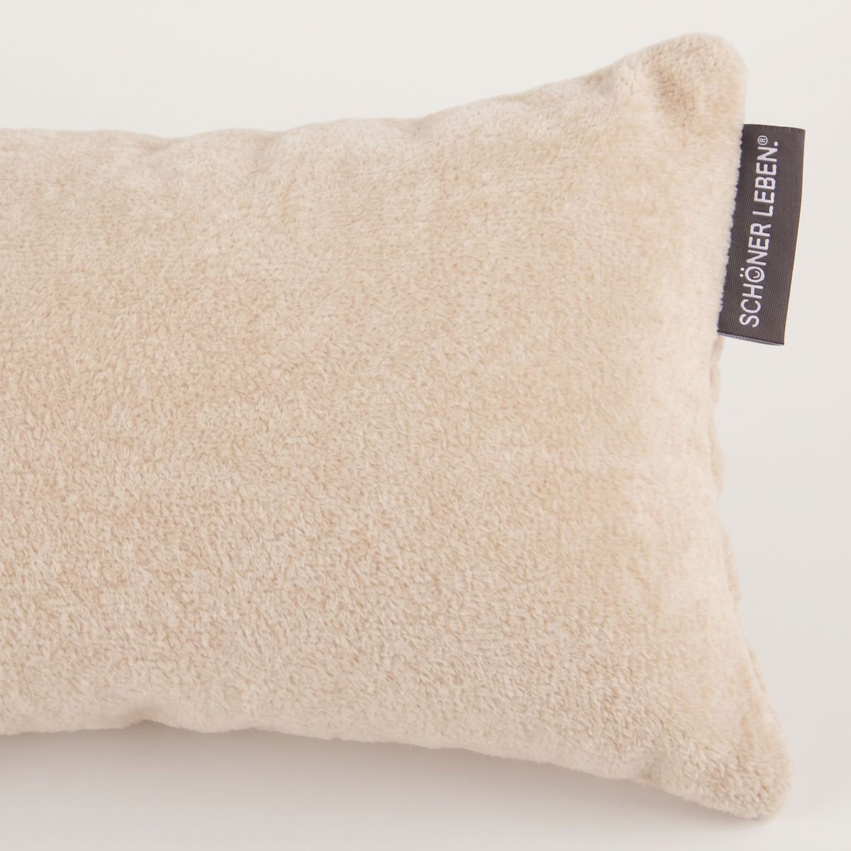 Nahaufnahme eines cremefarbenen Kissens aus Soft Teddy Stoff mit SCHÖNER LEBEN. Etikett