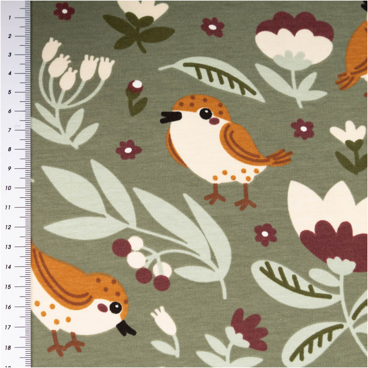 Stoff mit grünen Vogel- und Blumenmotiven, Maßband am Rand