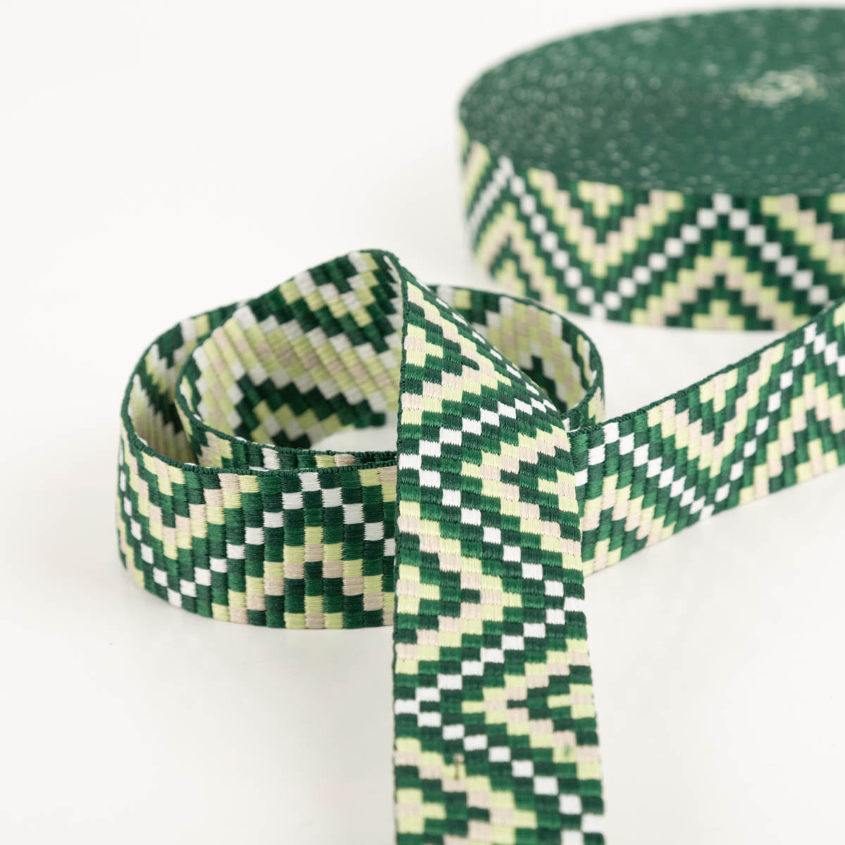 Gurtband Zickzack Chevron grün lindgrün weiß 3,8cm Breite grünes Gurtband mit Zickzackmotiv liegt in Schlaufen, Rolle im Hintergrund