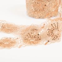 Nahaufnahme einer altrosa Borte mit kupferfarbenen Pailletten und Perlen, Blumenmuster, teils gerollt
