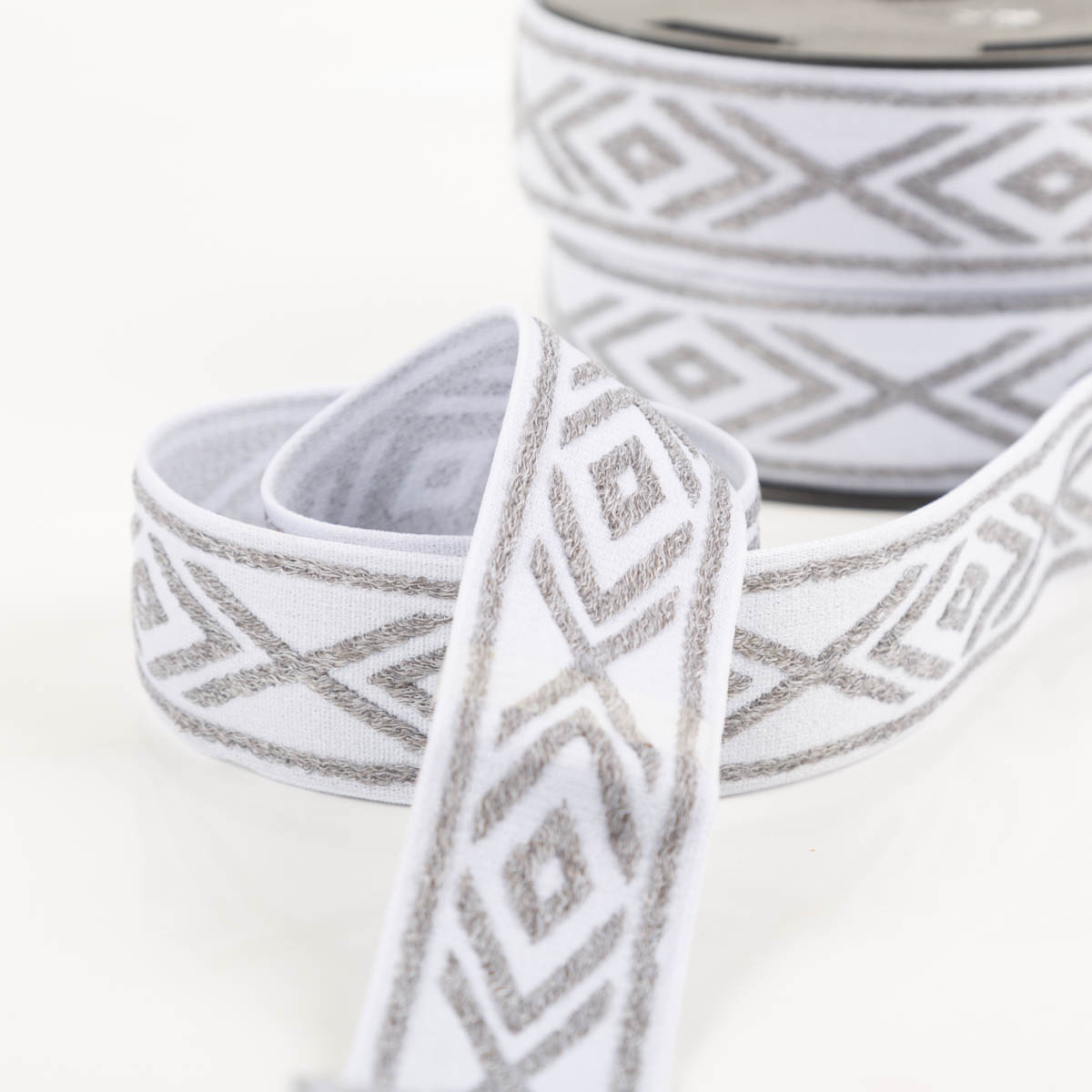 Gummiband Glitzer Rauten geometrisch weiß silber 4cm Breite glänzendes Elastikband in Weiß mit silbernen Rauten, dekorativ in Kurven gelegt, Nahaufnahme