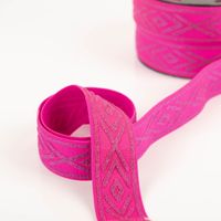 elastisches Band mit silbernen Rauten auf pinkem Stoff, eine Lage locker gelegt, Rolle im Hintergrund