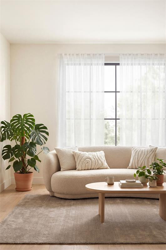 Weiße transparente Vorhänge am Fenster eines hellen Wohnzimmers mit Sofa, Couchtisch und Pflanze