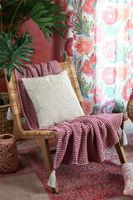 Decke Plaid Bellissima Zickzackmuster mit Quasten fuchsia rosa weiß 125x150cm Plaid Bellissima über einem Rattansessel vor roter Wand, daneben Grünpflanzen und bunte Kissen